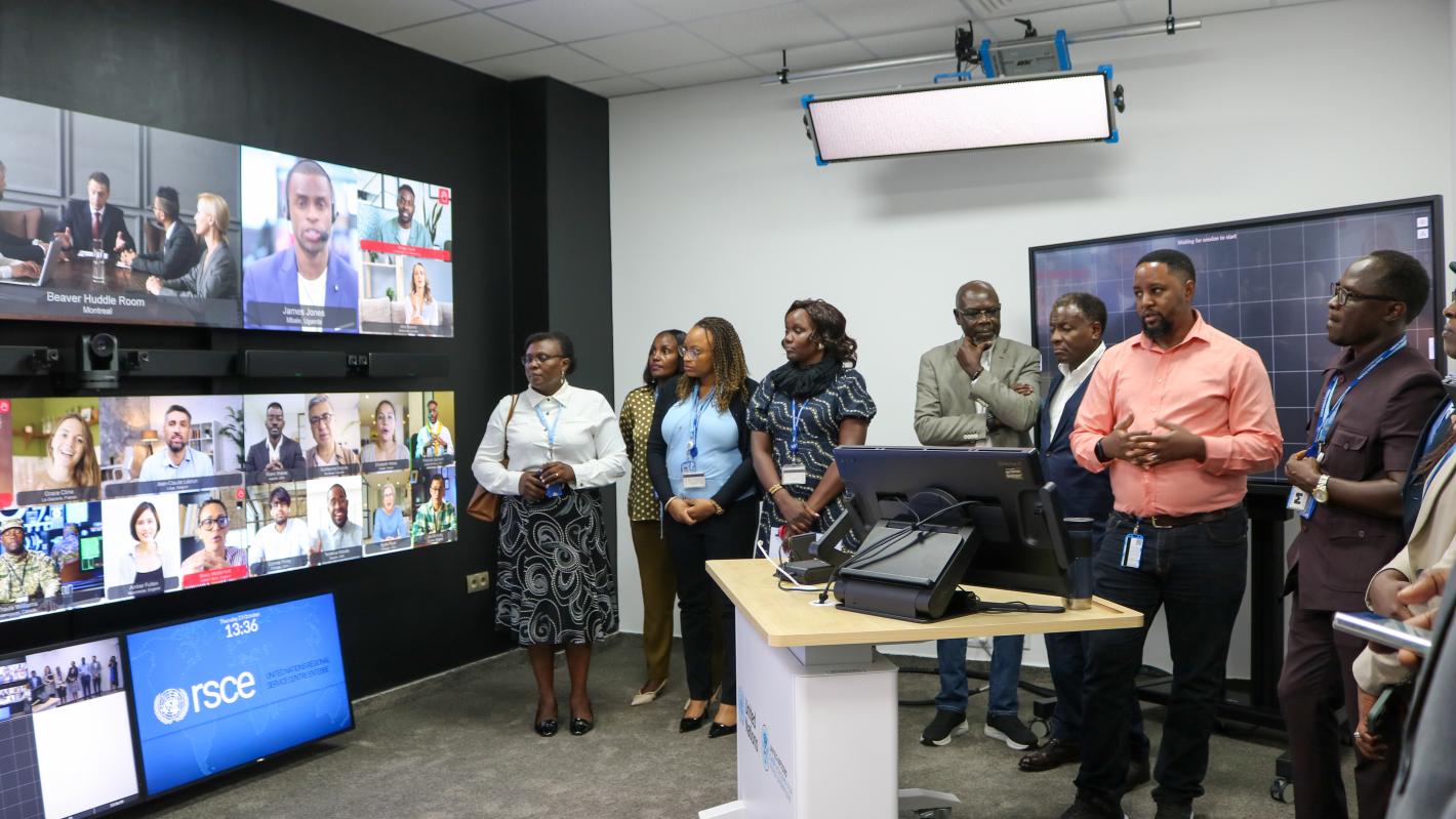 A group of people look at multiple TV screens with video conference calls displaying